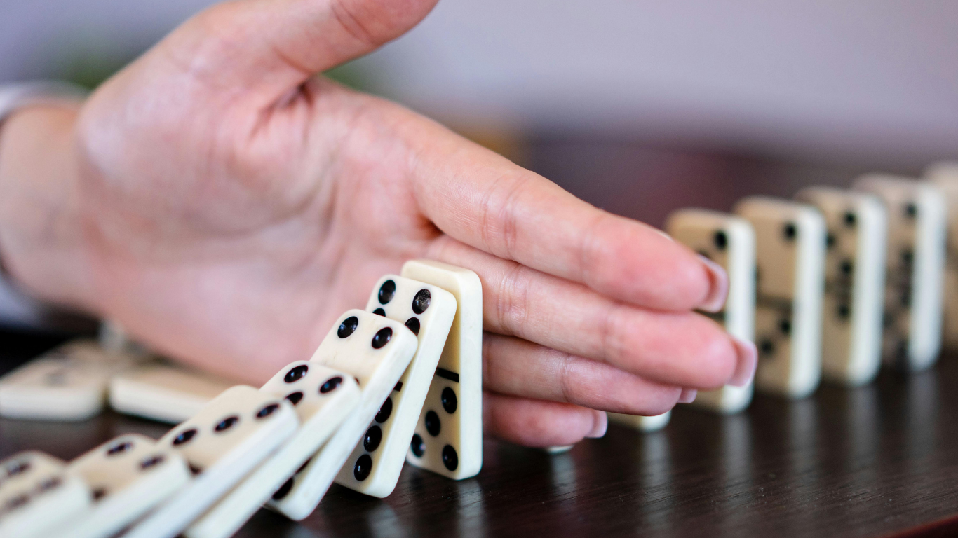 person's hand stopping dominos from falling